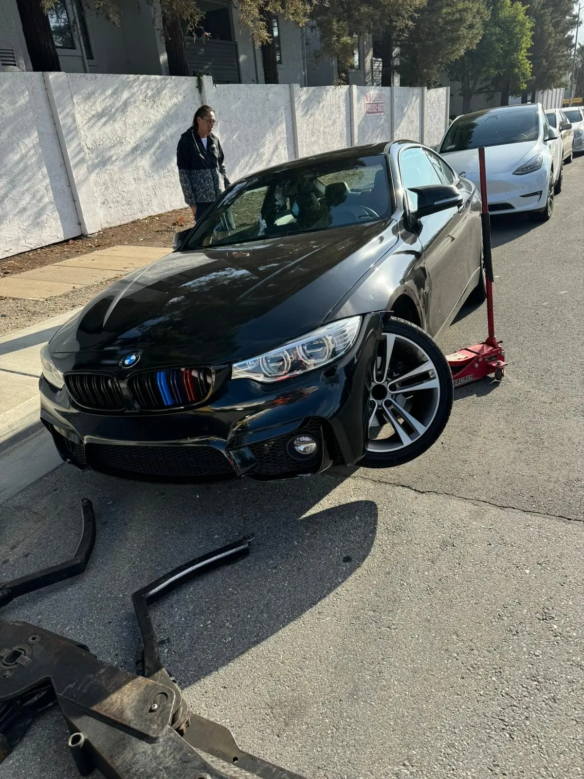 Damaged BMW at the curb with its front bumper off, before a Guerra Towing tow