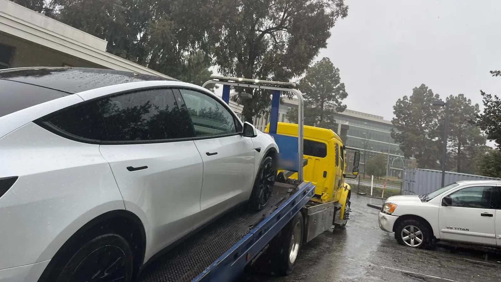 Un Tesla Model Y asegurado en una plataforma de remolque de Guerra Towing frente a un complejo de oficinas, el tipo de servicio que se solicita en Santa Clara