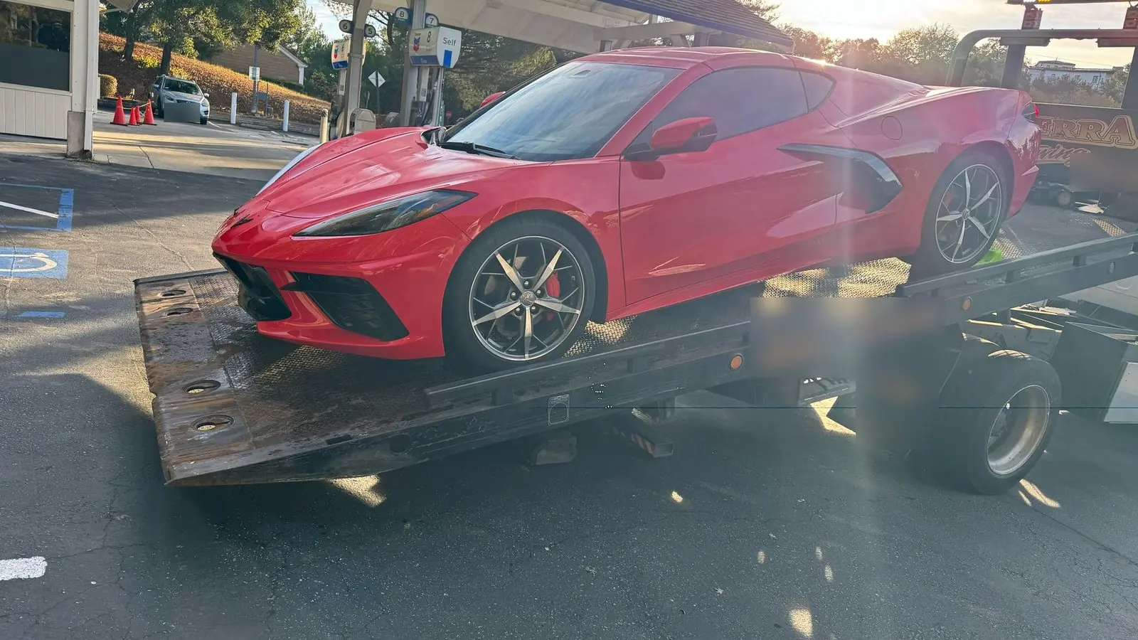 Grúa de plataforma de Guerra Towing al amanecer, con un auto deportivo Corvette rojo cargado en la plataforma; el morro bajo no toca la rampa