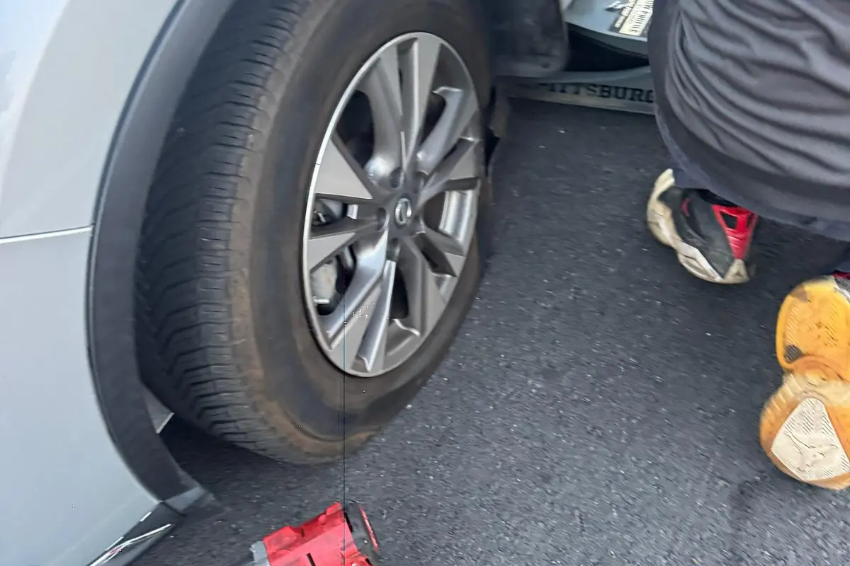 Un miembro del equipo de Guerra Towing junto a un cubo de rueda, con una llave de impacto y un gato, al costado de la carretera en San José