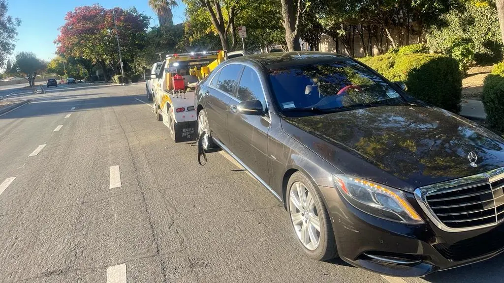 Una grúa con elevador de ruedas de Guerra Towing está enganchando un sedán Mercedes negro en un tranquilo bulevar arbolado